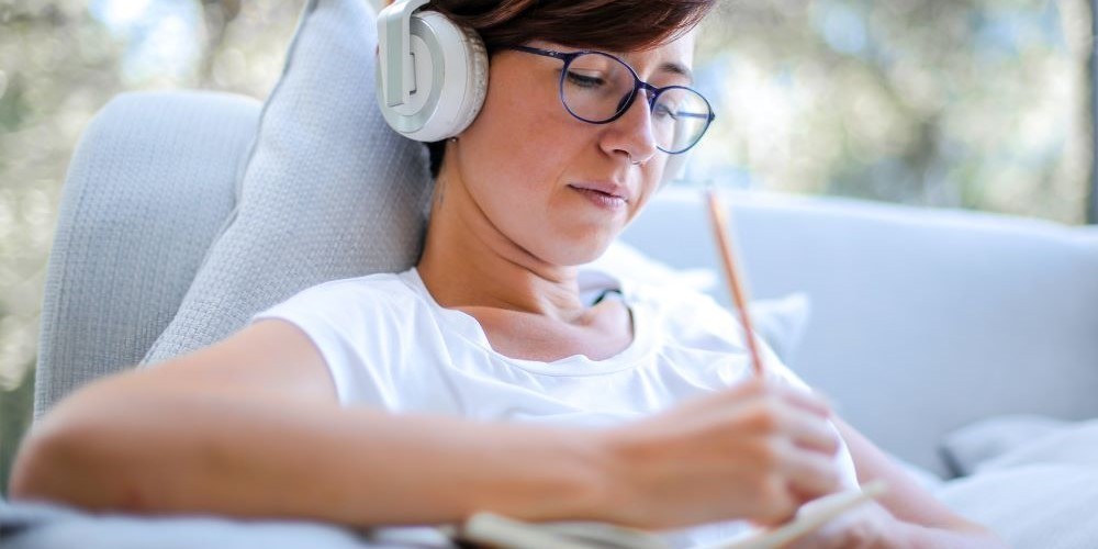 Blogbeitrag Schreiben mit Musik - Bild zeigt eine Frau mit Kopfhörern beim Schreiben.