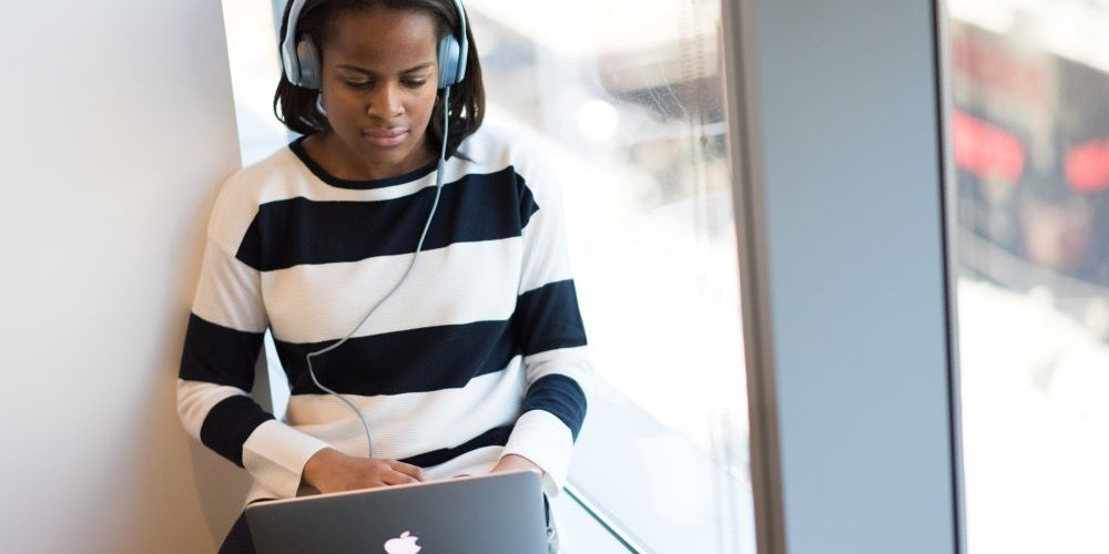 Blogbeitrag zum Thema Schreiben mit Musik. Bild zeigt eine Frau mit Kopfhörern, die am Laptop tippt.