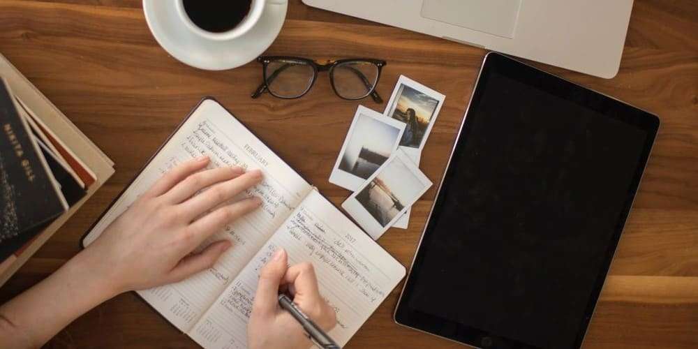 Bild zum Blogbeitrag Erfahrungsbericht Gateless Writing, zeigt schreibende Hand, Tisch, Notizbuch, Laptop
