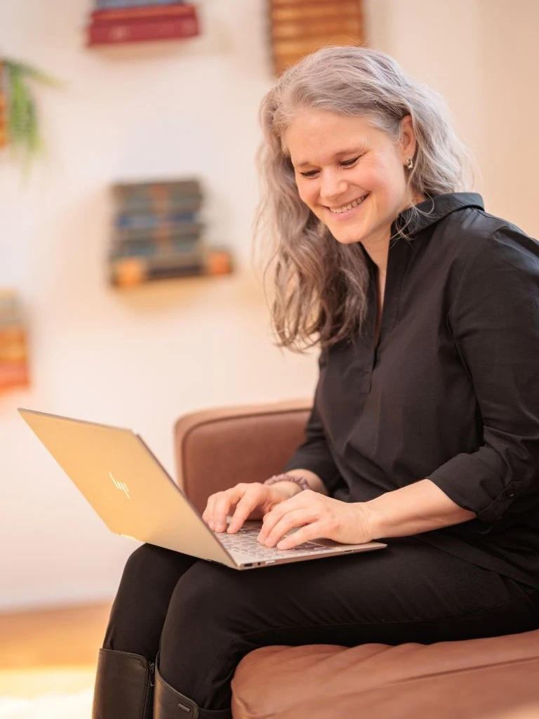 Christine Kämmer leitet Schreibworkshops in Präsenz, hier mit Laptop auf dem Sofa.