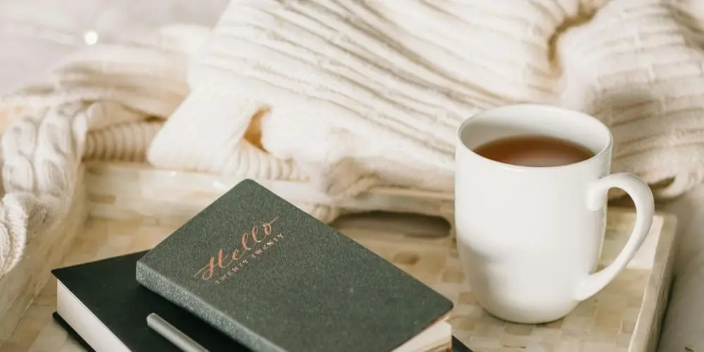 Bild zum Blogbeitrag "Morgenseiten", zeigt eine Tasse, ein Journal und ein Bett.