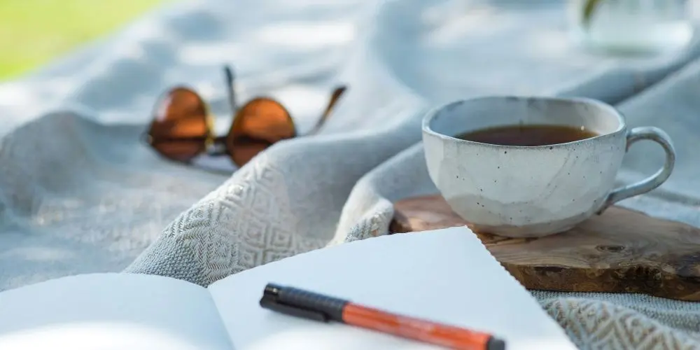 Bild zum Blogbeitrag "Impulse für kreatives Schreiben", zeigt Notizbuch, Teetasse und Sonnenbrille.